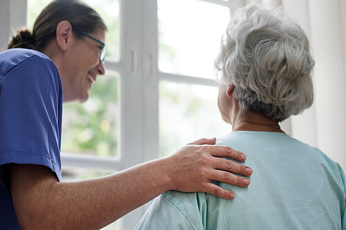 Woman in scrubs with hand on shoulder of older woman